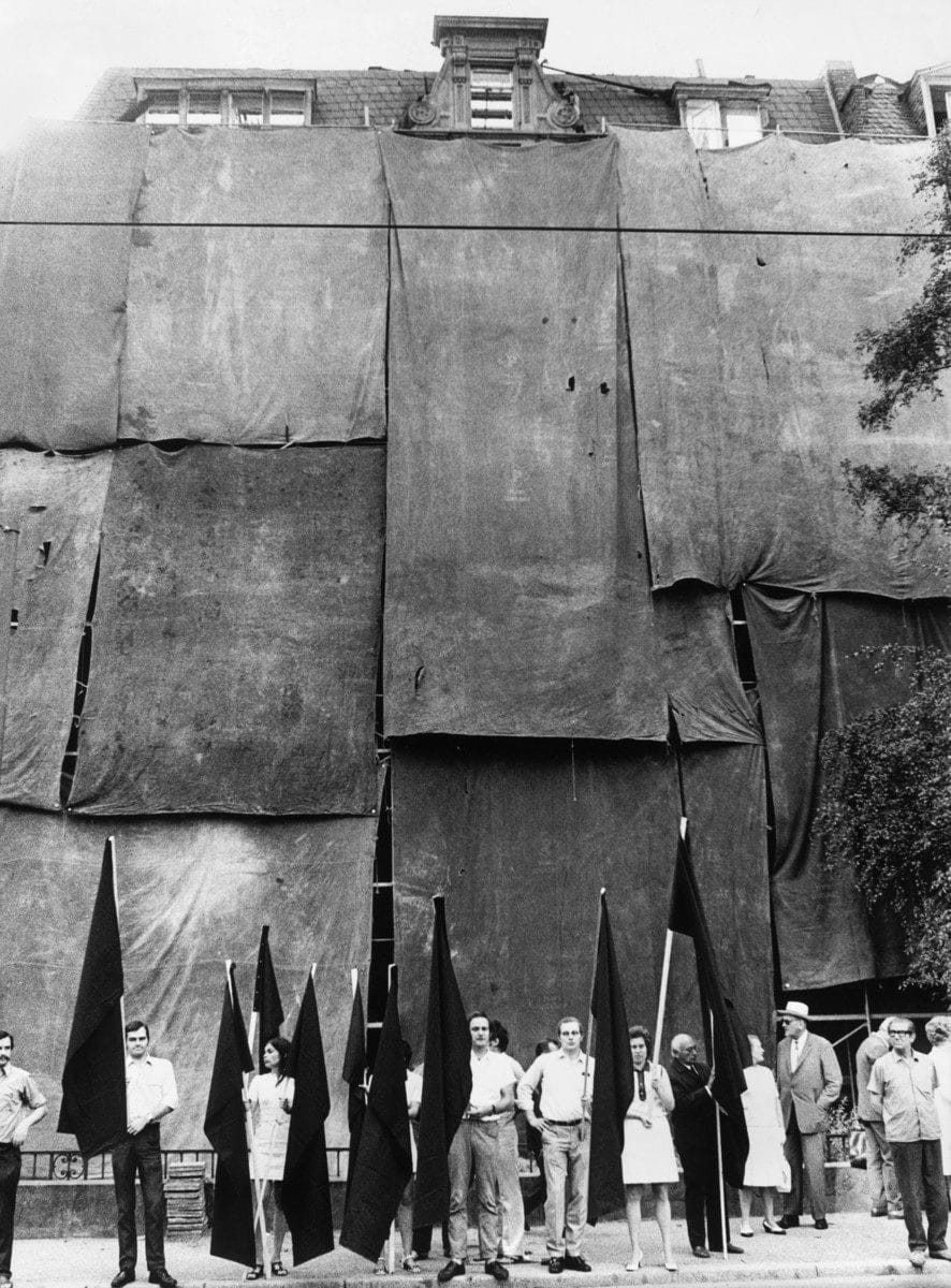 "Schwarzfahnendemonstration” des Westendvereins gegen Immobilienspekulation und Häuserabbruch im Westend, August 1970, Abisag Tüllmann, bpk-Archiv, Inv. Nr. Tü W70/059-32: Menschen mit schwarzen Flaggen vor einem verhängten Haus.